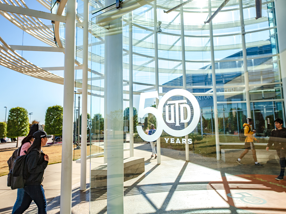 Students walk past a UTD monogram marking the school's 50th anniversary.