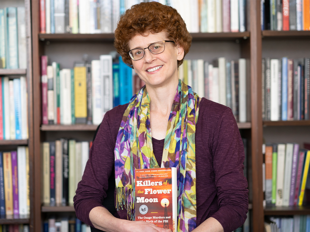 Woman holding book in front of bookshelf