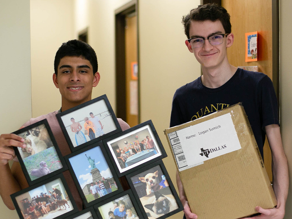 Male students holding belongings in room as they unpack