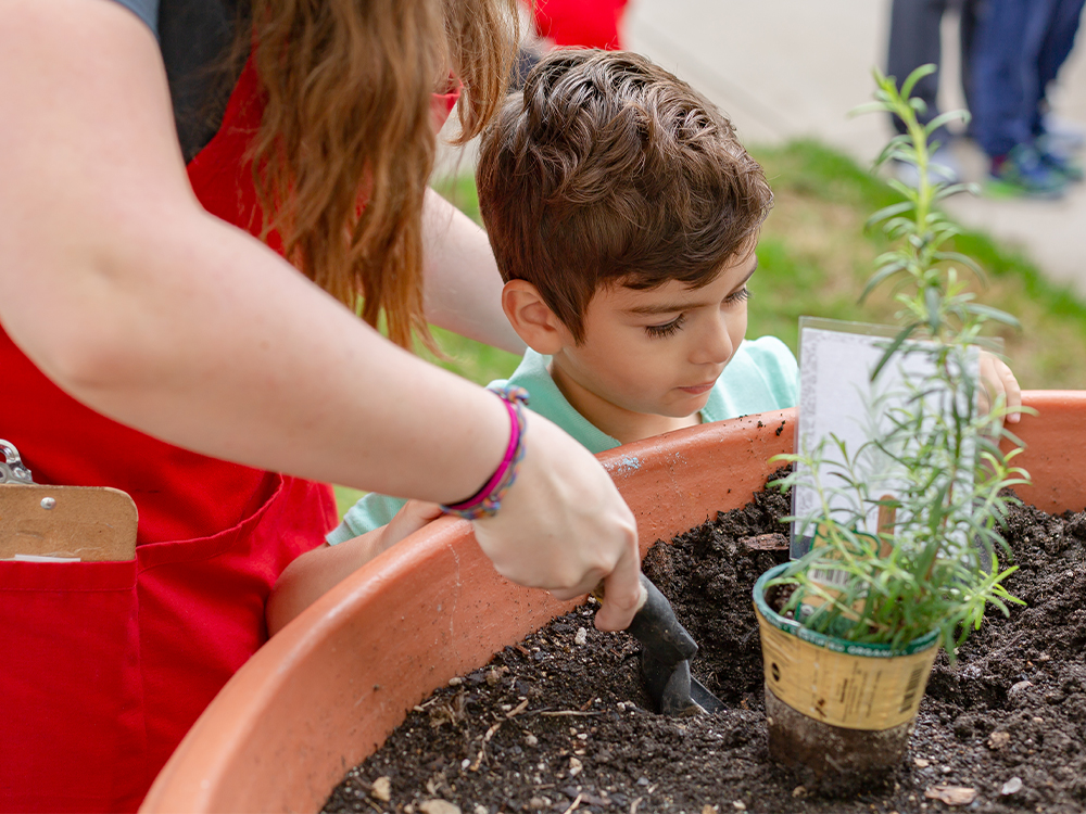 Young child watches as college student demonstrates how to plant a flower